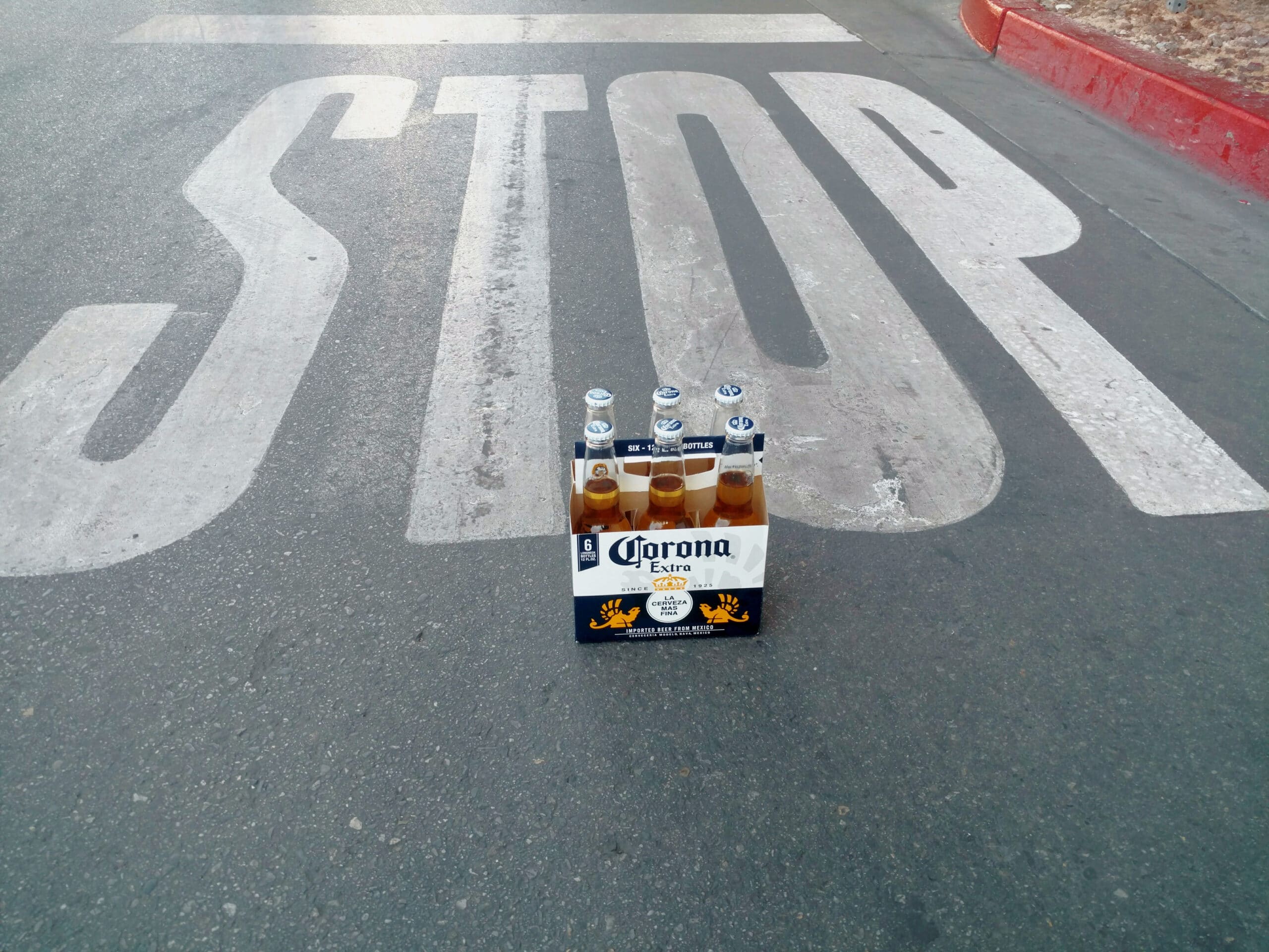 A pack of Corona beer bottles sits in front of a road Stop signal, indicating drunk driving prevention.