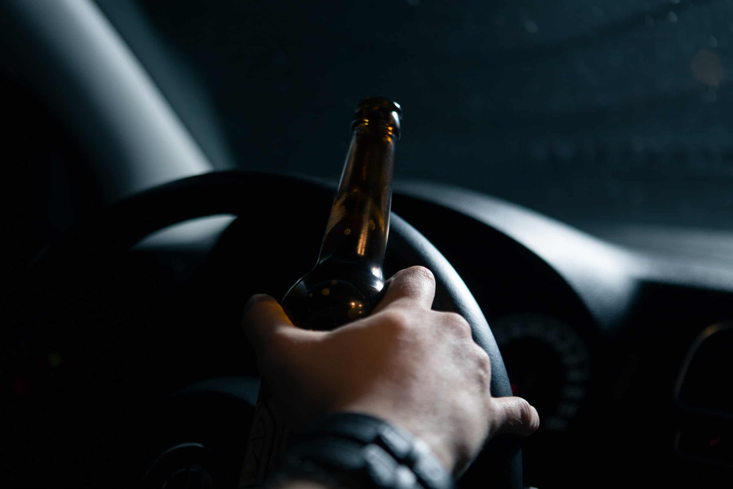 A driver behind the wheel with a beer bottle, suggesting drunk driving.